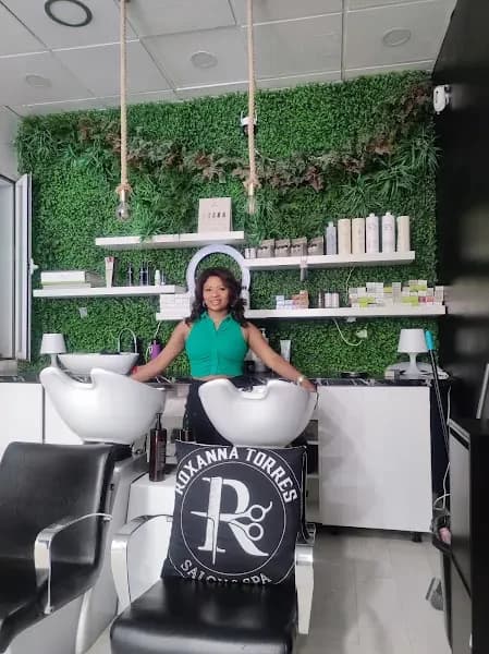 Interior del salón Roxanna Torres: lavacabezas, estanterías de productos y pared vegetal